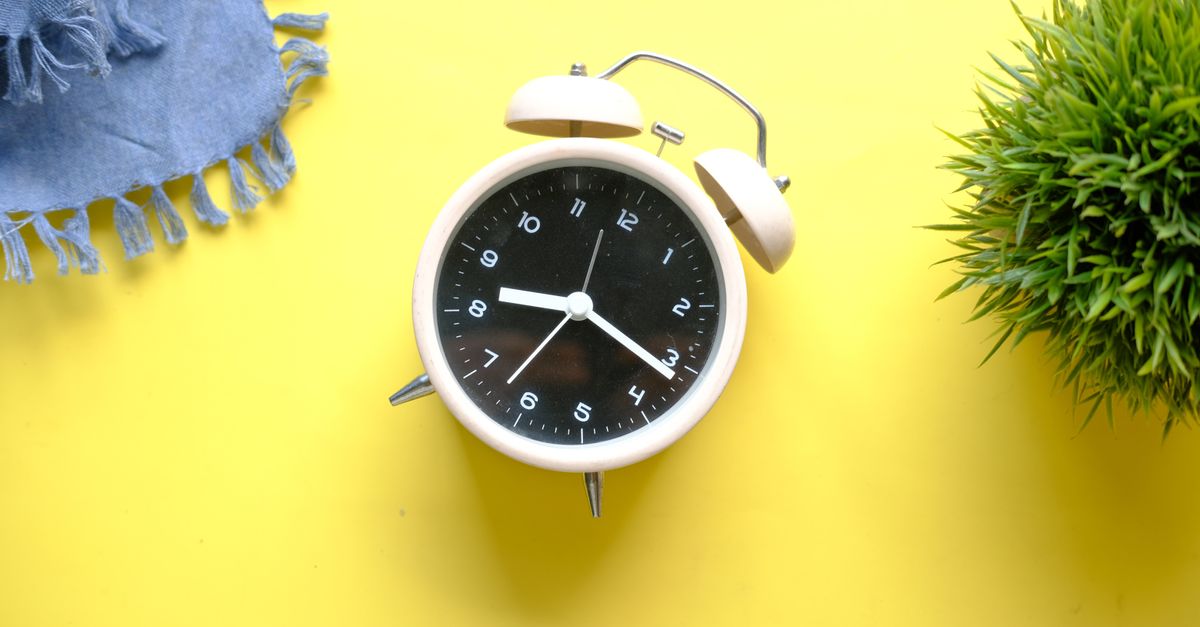 A vintage-style alarm clock on a vibrant yellow surface with a denim cloth and green plant.